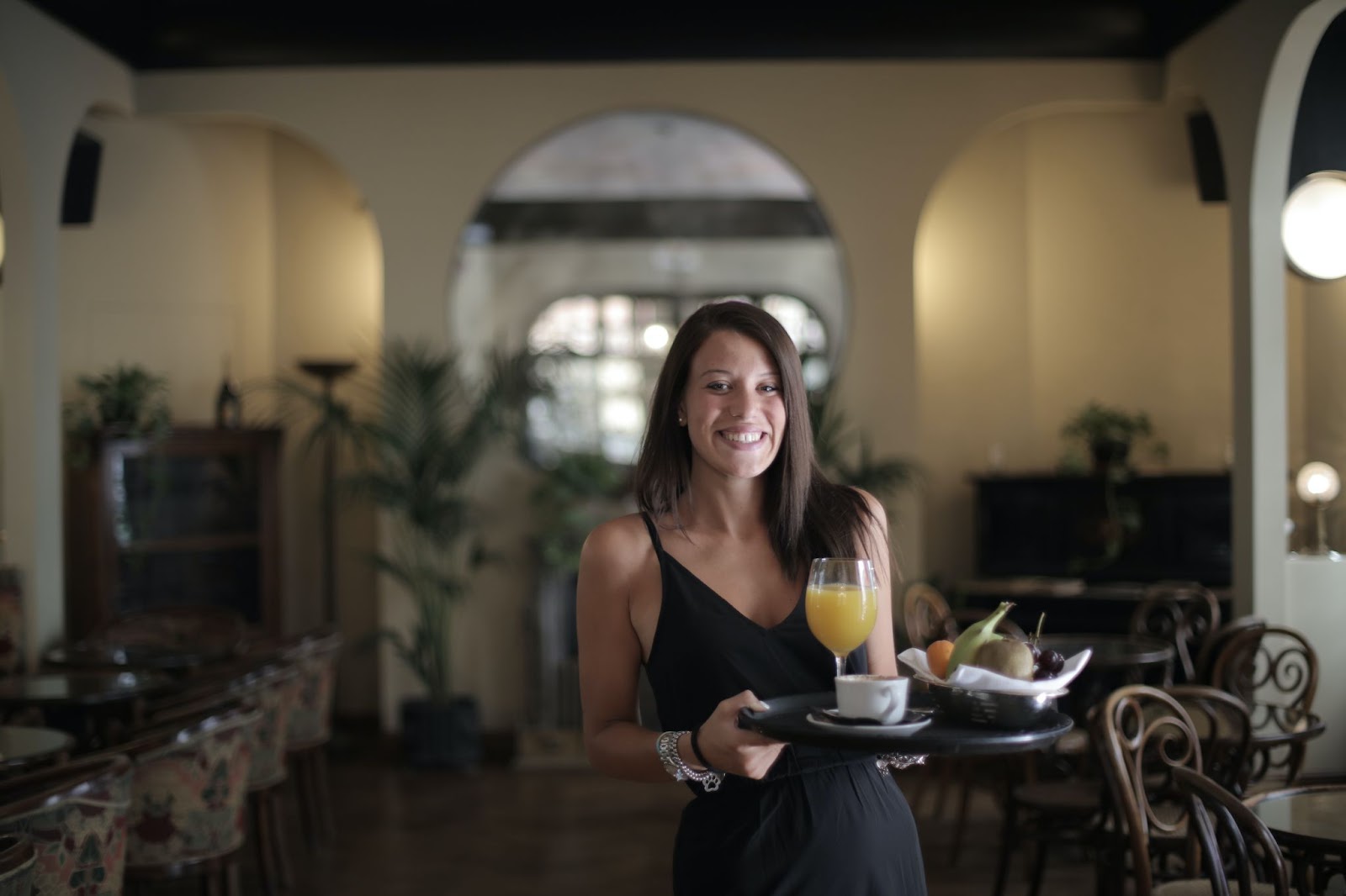 Restaurant manager pauses with a tray of fresh fruit, coffee and juice, wearing a grateful, welcoming smile.