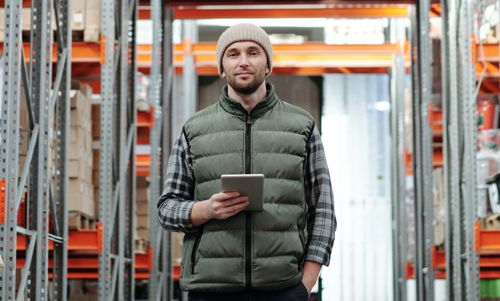 A confident worker, holding a tablet computer and dressed appropriately for a walk-in freezer, stands in their supermarket's commissary warehouse, ready to guide a direct store delivery back to the distribution center.