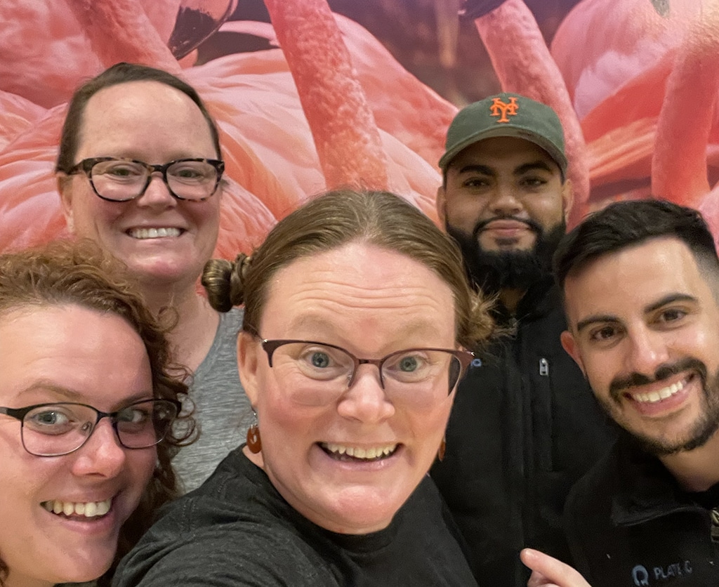 After-hours team selfie in front of a giant photo of flamingos. Happy Plate IQ employees looking forward to dinner and rest before the next conference day.